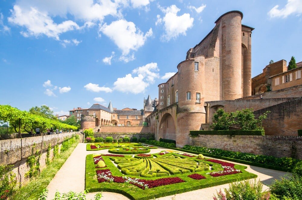 Palais imposant sur la droite en briques rouges et jardin de parterres de fleurs de l'Archevêché à Albi