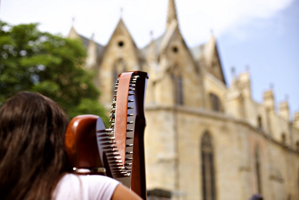 Une femme porte une harpe sur l'épaule en gros plan se dirigeant vers la cathédrale.