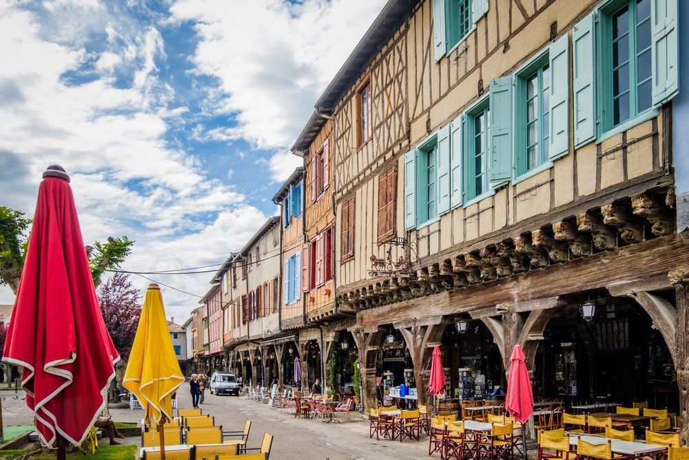 Enfilade de maisons à colombages aux volets colorés sur la place de Mirepoix.