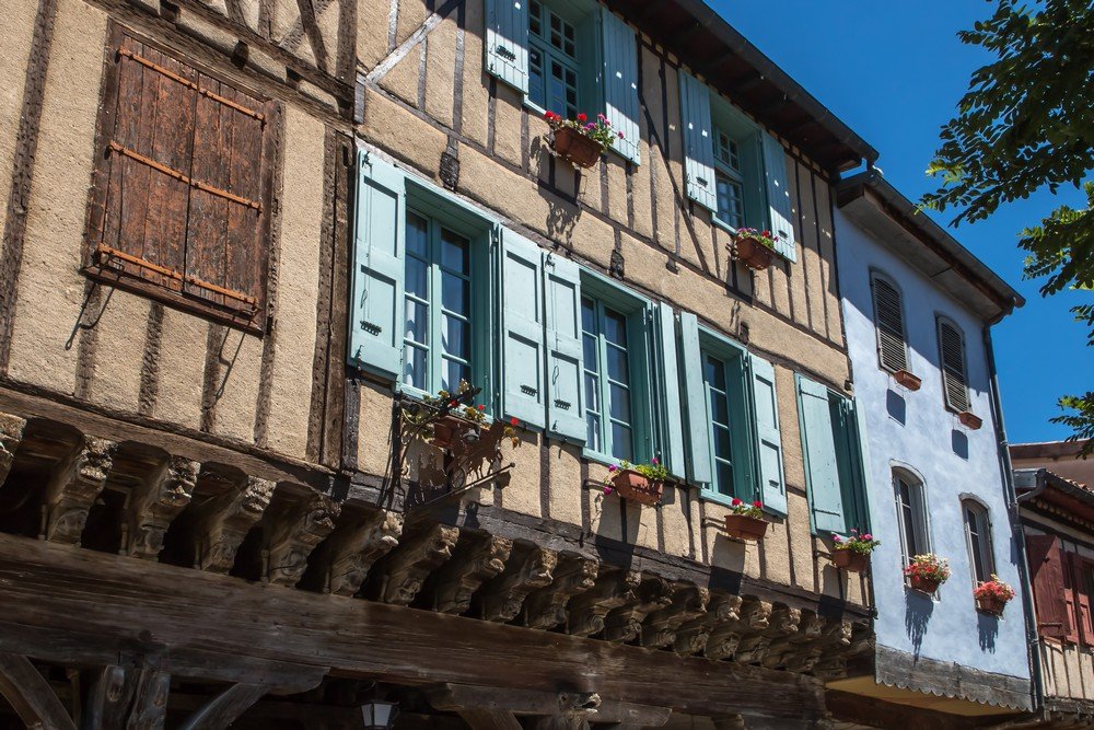 Jolie maison à colombages aux volets bleu ciel avec des poutres sculptées au premier niveau.