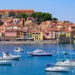 Village de Collioure photographié depuis la baie, on y voit des bateaux au premier plan puis l'église Notre Dame des Anges et le village de pêcheurs